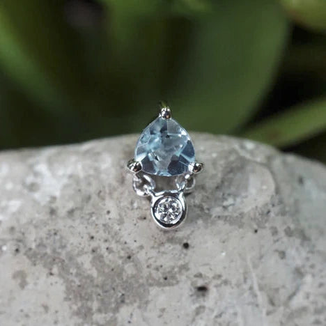 White Gold ring with a blue gemstone on a stone surface with greenery in the background
