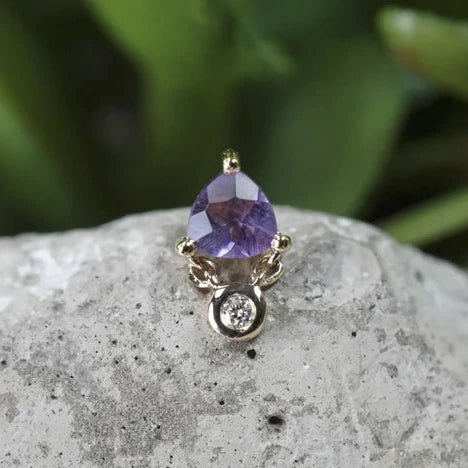 Gold ring with a purple gemstone on a rock with green foliage in the background
