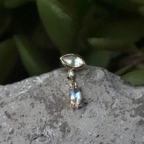 Gold earring with a gemstone on a stone surface with greenery in the background