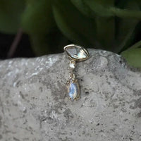 Gold earring with a gemstone on a stone surface with green leaves in the background