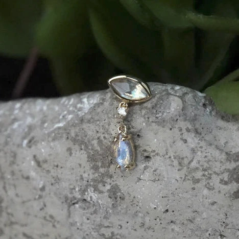 Gold earring with a gemstone on a stone surface with green leaves in the background
